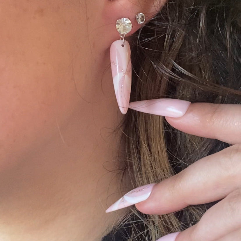 Close-up of an ear with pink nail polish and earrings.